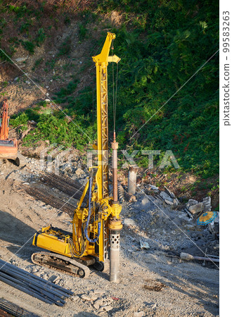 The yellow pile driver drives the foundation piles at the construction site. The yellow pile driver drives the foundation piles at the construction site. 99583263