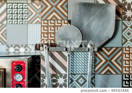 Pizza tools hang on the wall next to the oven. 99583486