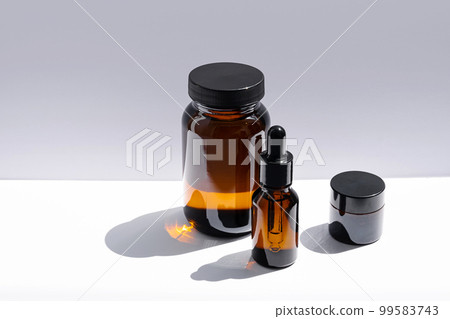 Amber glass cosmetic bottles with reflections on white surface. 99583743