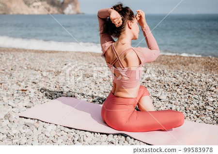 Middle aged well looking woman with black hair, fitness instructor in leggings and tops doing stretching and pilates on yoga mat near the sea. Female fitness yoga routine concept. Healthy lifestyle 99583978