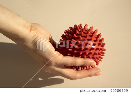 Spiked red rubber massage ball in a woman's hand. Ball for recovery and rehabilitation or for relaxation and massage. Fitness equipment. Myofascial release concept. 99586569