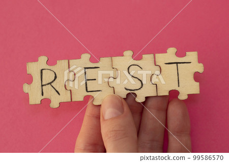 Rest inscription on assembled wooden puzzles in a woman's hand on a red background. 99586570