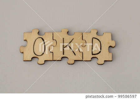 Text lettering OCD handwritten on wooden puzzles. Assembled abbreviation on blue background. 99586597