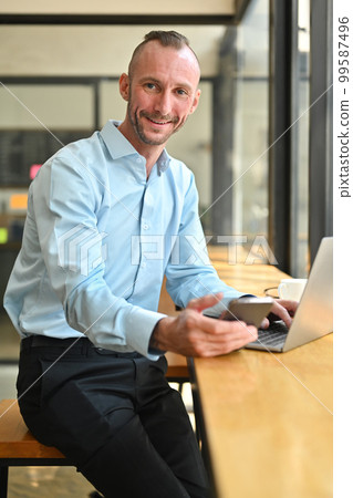 Positive caucasian businessman holding smart phone and looking confidently to camera Positive caucasian businessman holding smart phone and looking confidently to camera 99587496