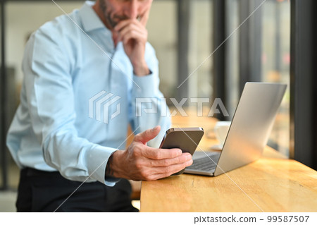 Cropped shot of smiling male worker communicating in social media, sitting wooden counter in front of laptop Cropped shot of smiling male worker communicating in social media, sitting wooden counter in front of laptop 99587507