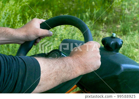 Male hands of the driver holding the steering wheel of a tractor, lawn mower Male hands of the driver holding the steering wheel of a tractor, lawn mower 99588925