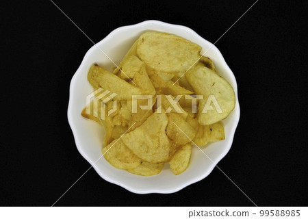 Potato chips in a white plate. Delicious pieces of chips. Salty fast food. 99588985