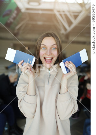 young beautiful woman is holding travel tickets and passports, happy girl looking at camera in airport terminal. summer travel vacation young beautiful woman is holding travel tickets and passports, happy girl looking at camera in airport terminal. summer travel vacation 99590479
