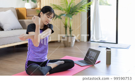 Woman looking at yoga teacher on laptop and doing light exercise in the living room at home, Watch live teaching or VDO on laptop, Dumbbells and a protein shake or bottle of water, Healthy exercise. Woman looking at yoga teacher on laptop and doing light exercise in the living room at home, Watch live teaching or VDO on laptop, Dumbbells and a protein shake or bottle of water, Healthy exercise. 99590753