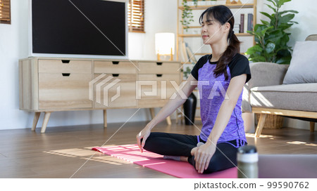 Woman looking at yoga teacher on laptop and doing light exercise in the living room at home, Watch live teaching or VDO on laptop, Dumbbells and a protein shake or bottle of water, Healthy exercise. 99590762