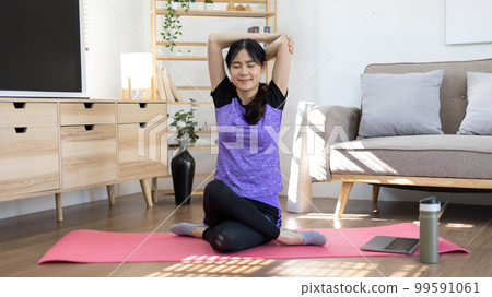 Beautiful healthy woman practicing yoga, Stretch or warm up before exercising, Calming the mind and meditating in her living room, Dumbbells and a protein shake or bottle of water, Healthy exercise. Beautiful healthy woman practicing yoga, Stretch or warm up before exercising, Calming the mind and meditating in her living room, Dumbbells and a protein shake or bottle of water, Healthy exercise. 99591061