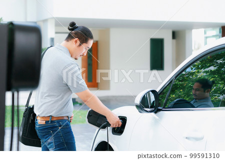 Progressive asian man recharge his EV car at home charging station. 99591310