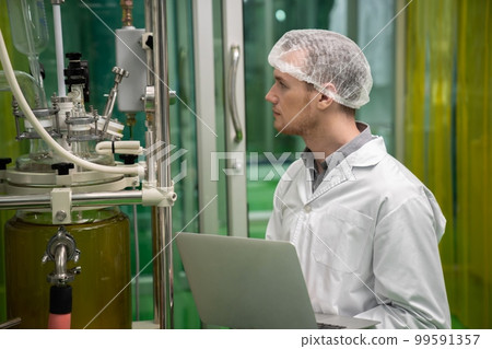 Apothecary scientist recording data from CBD oil extractor in laboratory. 99591357