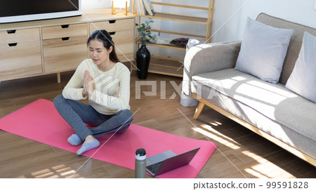 Beautiful healthy woman practicing yoga, Stretch or warm up before exercising, Calming the mind and meditating in her living room, Dumbbells and a protein shake or bottle of water, Healthy exercise. Beautiful healthy woman practicing yoga, Stretch or warm up before exercising, Calming the mind and meditating in her living room, Dumbbells and a protein shake or bottle of water, Healthy exercise. 99591828