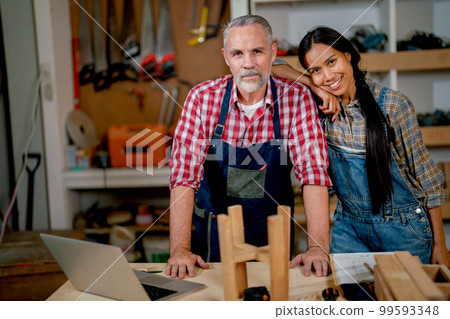 Carpenter lovers stand closely together and look at camera during work in workplace Carpenter lovers stand closely together and look at camera during work in workplace 99593348