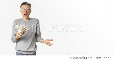 Portrait of surprised middle-aged man in glasses and gray sweater, holding money, winning lottery, standing over white background Portrait of surprised middle-aged man in glasses and gray sweater, holding money, winning lottery, standing over white background 99593562
