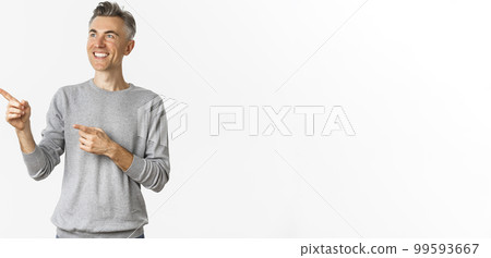 Image of smiling handsome middle-aged man looking at logo, pointing fingers left and showing advertisement, standing over white background 99593667