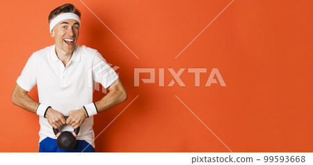 Concept of workout, gym and lifestyle. Image of handsome middle-aged guy doing sport exercises, lifting kettlebell and smiling, standing over orange background 99593668