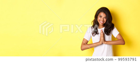 Image of cute african american woman, saying thank you and smiling, press hands together to express gratitude, standing over yellow background Image of cute african american woman, saying thank you and smiling, press hands together to express gratitude, standing over yellow background 99593791