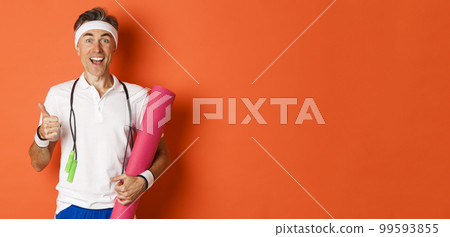 Concept of workout, gym and lifestyle. Cheerful middle-aged fitness guy, holding skipping rope and yoga mat, showing thumbs-up and smiling satisfied, standing over orange background 99593855