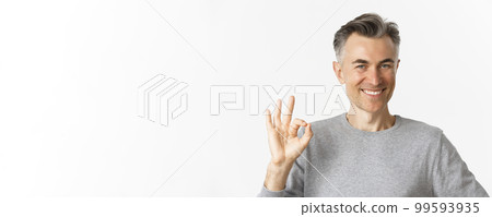 Close-up of handsome middle-aged man, showing okay sign and smiling, guarantee quality, assure that everything good, standing over white background 99593935