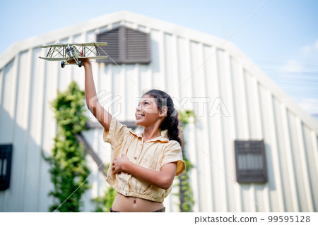 Asian girl enjoy to play with plane model in home garden or yard with warm light and blue sky Asian girl enjoy to play with plane model in home garden or yard with warm light and blue sky 99595128
