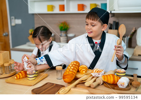 Boy and little girl wear chef cloth have fun in kitchen with bread and tools during practice 99595134