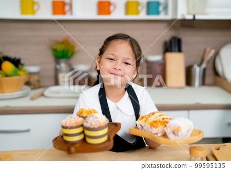 Lovely little girl hold plate with cake and cupcake and present to camera with happy face 99595135