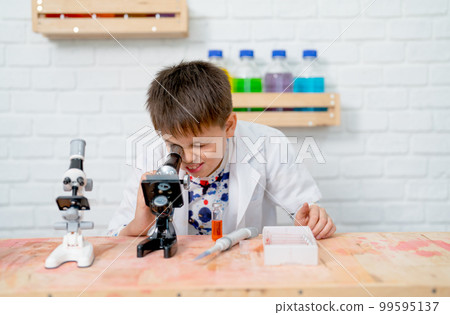 Young boy wear lab gown and work with microscope in science class of school to practic Young boy wear lab gown and work with microscope in science class of school to practic 99595137