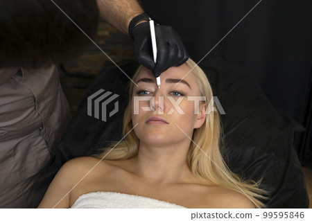 Doctor draws correction, lifting lines on female face,nose in examination room. Preparing to botox,beauty injection, surgery procedure in clinic. Woman lying on couch. Cosmetology, aesthetic medicine 99595846