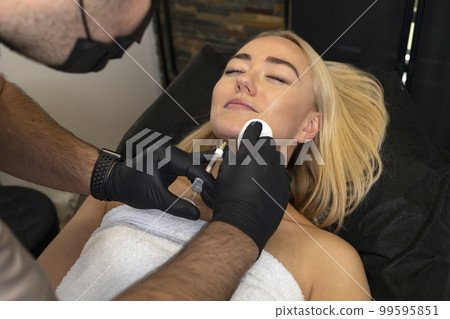 Physician adds volume to woman's chin with filler, injection. White female lying on couch. Beauty physician holds syringe near girl's face.Chin reshaping, augmentation.Cosmetologist,aesthetic medicine Physician adds volume to woman's chin with filler, injection. White female lying on couch. Beauty physician holds syringe near girl's face.Chin reshaping, augmentation.Cosmetologist,aesthetic medicine 99595851