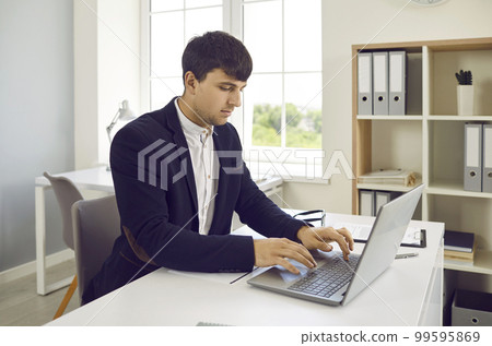 Young man working in office, sitting at his desk and typing on modern laptop computer 99595869