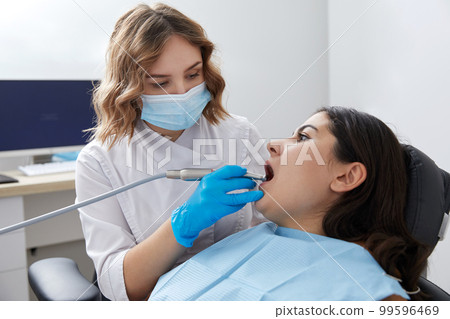 Dentist drilling tooth of female patient in dental chair 99596469