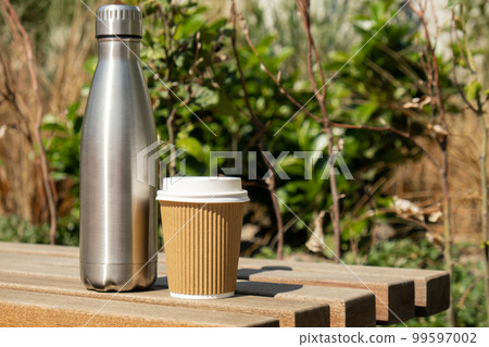 Reusable steel thermo water bottle on wooden bench with paper cup. Sustainable lifestyle. Plastic free zero waste free living. Go green Environment protection. Health-conscious Reusable steel thermo water bottle on wooden bench with paper cup. Sustainable lifestyle. Plastic free zero waste free living. Go green Environment protection. Health-conscious 99597002