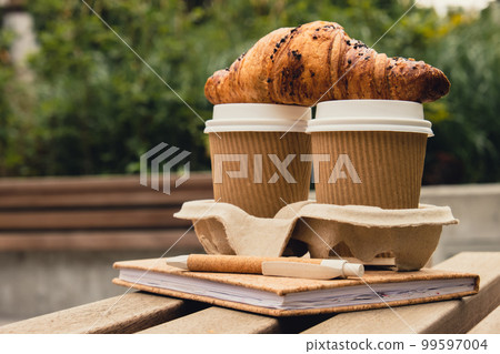 Fresh baked chocolate croissant on Two paper cups with lid for tea to go. Empty paper notebook. Freelancer's place of work. Study and work online. Remote business education. Making plans for next week Fresh baked chocolate croissant on Two paper cups with lid for tea to go. Empty paper notebook. Freelancer's place of work. Study and work online. Remote business education. Making plans for next week 99597004