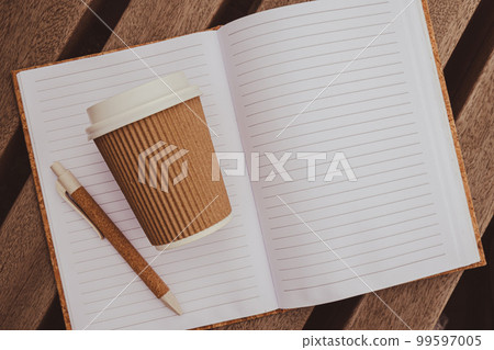 Eco recycling paper cup with coffee or tea on kraft paper with empty paper notebook on wooden bench. Concept of study work outdoors. Take away coffee to go. Copy space for text. Disposable Cardboard Eco recycling paper cup with coffee or tea on kraft paper with empty paper notebook on wooden bench. Concept of study work outdoors. Take away coffee to go. Copy space for text. Disposable Cardboard 99597005