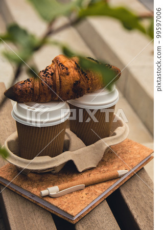Fresh baked chocolate croissant on Two paper cups with lid for tea to go. Empty paper notebook. Freelancer's place of work. Study and work online. Remote business education. Making plans for next week Fresh baked chocolate croissant on Two paper cups with lid for tea to go. Empty paper notebook. Freelancer's place of work. Study and work online. Remote business education. Making plans for next week 99597006