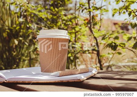 Eco recycling paper cup with coffee or tea on kraft paper with empty paper notebook on wooden bench. Concept of study work outdoors. Take away coffee to go. Copy space for text. Disposable Cardboard Eco recycling paper cup with coffee or tea on kraft paper with empty paper notebook on wooden bench. Concept of study work outdoors. Take away coffee to go. Copy space for text. Disposable Cardboard 99597007