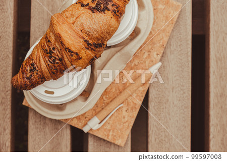 Fresh baked chocolate croissant on Two paper cups with lid for tea to go. Empty paper notebook. Freelancer's place of work. Study and work online. Remote business education. Making plans for next week 99597008