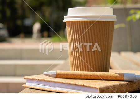 Eco recycling paper cup with coffee or tea on kraft paper with empty paper notebook on wooden bench. Concept of study work outdoors. Take away coffee to go. Copy space for text. Disposable Cardboard Eco recycling paper cup with coffee or tea on kraft paper with empty paper notebook on wooden bench. Concept of study work outdoors. Take away coffee to go. Copy space for text. Disposable Cardboard 99597010