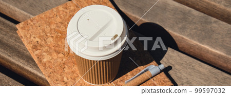 Eco recycling paper cup with coffee or tea on kraft paper with empty paper notebook on wooden bench. Concept of study work outdoors. Take away coffee to go. Copy space for text. Disposable Cardboard Eco recycling paper cup with coffee or tea on kraft paper with empty paper notebook on wooden bench. Concept of study work outdoors. Take away coffee to go. Copy space for text. Disposable Cardboard 99597032