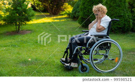 Unhappy elderly woman crying while sitting in a wheelchair on a walk outdoors.  99598521