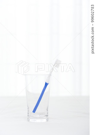 A toothbrush with a blue handle is stuck in a glass cup 99602783