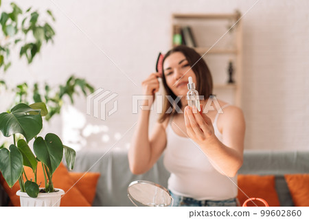 Lady holding glass bottle with pipette in front of her and combing her hair 99602860
