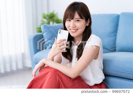 A young woman using a smartphone in a bright living room A young woman using a smartphone in a bright living room 99607072
