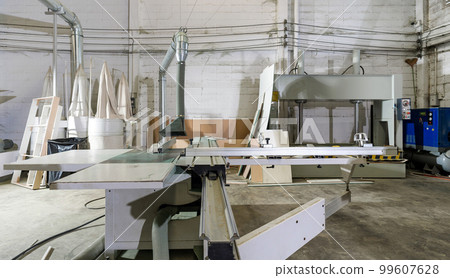 A large sliding table saw machine with dust hood in industrial factory producing wooden furniture parts. A large sliding table saw machine with dust hood in industrial factory producing wooden furniture parts. 99607628