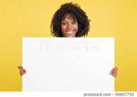 Woman with afro hair holding a blank panel while smiling 99607758