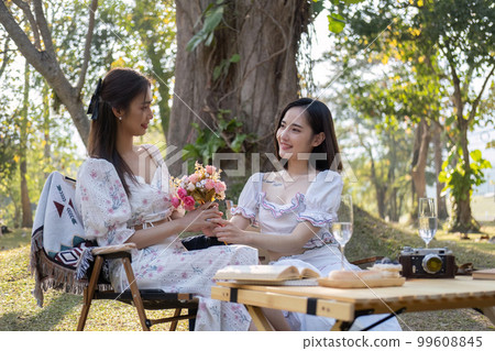 Gorgeous Asian woman giving a beautiful roses bouquet to her friend, having a special moment together in the park. female couple, lesbian, best friend, besties 99608845