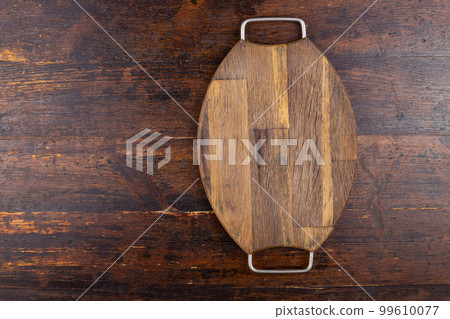 Wooden cutting board with iron handles on a wooden background. View from above Wooden cutting board with iron handles on a wooden background. View from above 99610077
