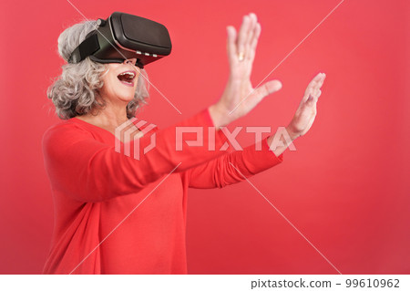 Mature woman gesturing while using a virtual reality goggles Mature woman gesturing while using a virtual reality goggles 99610962